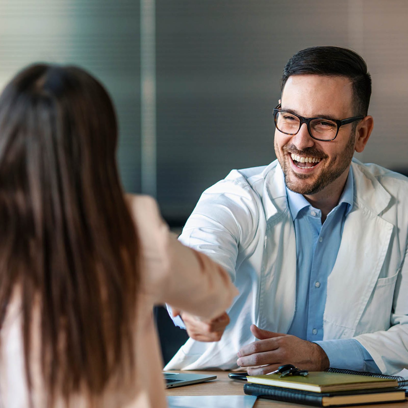 Doctor shaking hands with woman. Female patient visiting health professional. They are in hospital. Cropped shot of a handsome young male doctor and his patient shaking hands in the hospital